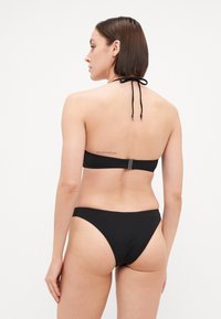 Svart bikini med halterneck og knytting, bandet topp og minimalt dekkende høytlivsbunn, laget av glatt stoff.