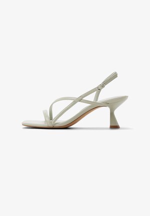 Gebroken-witte sandaal met bandjes, een vierkante neus, verstelbare gesp en een uitlopende kittenhak op een witte achtergrond.