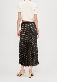 Witte cropped top met korte mouwen, gecombineerd met een zwarte geplooide maxi-jurk met een gouden patroon en een zwarte tailleband, gedragen met gouden hakken.