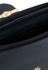 Marineblaue strukturierte Leder-Tasche mit einem Reißverschluss und goldfarbenen Beschlägen. Innen mit dunklem Stoff ausgekleidet, zusätzlich mit einer Tasche und Reißverschluss-Details.