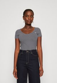 Camiseta de tirantes cortos con escote en forma de barco, con rayas en azul marino y blanco, combinada con jeans oscuros de tiro alto.