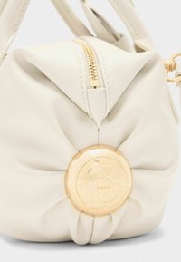 Borsa in pelle color crema con design annodato, dotata di una zip dorata e un accento a logo circolare dorato sul davanti.