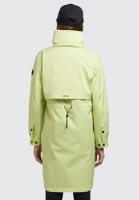 Svetlo zelena vodoodporna parka z visokim ovratnikom, prilagodljivim pasom in gumbnimi manšetami. Črni logo na hrbtu in eleganten, minimalističen dizajn.