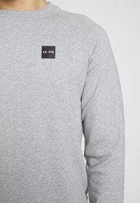 Felpa grigia realizzata in morbido cotone misto, con scollo rotondo e un piccolo patch con il logo LE FIX nero sul petto. Vestibilità rilassata.