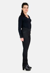 Top negro de manga larga con escote en V, combinado con pantalones negros texturizados que presentan sutiles detalles de hardware, y zapatos de tacón cerrados en negro.
