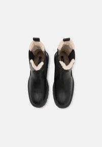 Bottines en cuir noir avec doublure en fausse fourrure beige, bout arrondi et tirant au dos, présentant des détails de couture sur la semelle.