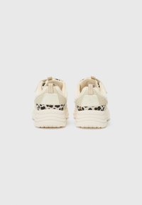 Helle beigefarbene Sneakers mit schwarzen Leopardenmuster-Akzenten, strukturiertem Material, gepolstertem Schaft und Zuglaschen an der Ferse für einfaches Anziehen.