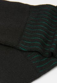 Czarna dzianina z poziomymi zielonymi paskami, o gładkiej teksturze i lekko prążkowanym wzorze. Miękki i elastyczny materiał.