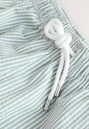 Tela a rayas en verde claro y blanco con una apariencia texturizada. Cuenta con un cordón ajustable con puntas de metal y cintura fruncida.