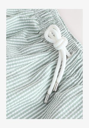 Lichtgroen-wit gestreept stof met een gestructureerd uiterlijk. Voorzien van een verstelbare trekkoord met metalen uiteinden en een taille met plooien.
