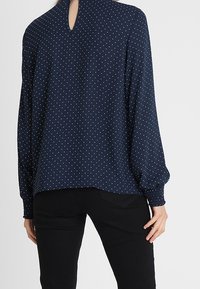 Marinblus med polka prickar, långa ärmar, elastiska manschetter och detaljer med nyckelhål på ryggen. Slätt tyg med avslappnad passform.