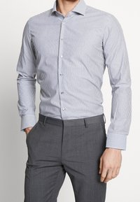 Men's button-up shirt, white with navy vertical stripes. Features a pointed collar, long sleeves with striped cuffs, and a fitted design.