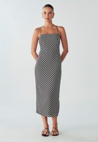 Čierno-biela midi šaty so vzorom, s tenkými ramienkami, priliehavým korzetom a rovnou siluetou. Nosí sa s minimalistickými čiernymi sandálmi.