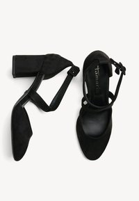 Paire de sandales à talon bloc en suède noir avec brides de cheville et boucles, une chaussure vue de dessus et l'autre de côté.