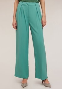 Breda byxor i tealtyg, med framfickor, en knäppt midja och slät textur. Kombineras med klackar med silverdetaljer.