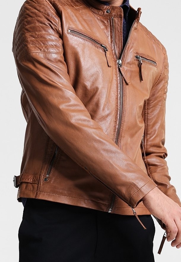 Giacca in pelle marrone con dettagli imbottiti sulle spalle, tasche anteriori con zip e design aderente. Texture liscia e linee eleganti.