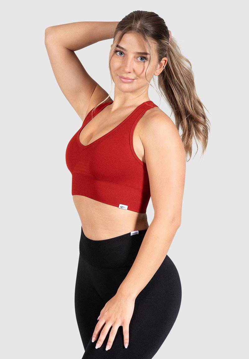 Sujetador deportivo rojo acanalado con tirantes anchos y diseño de escote en V. Combinado con mallas negras de cintura alta, que muestran una tela suave y una silueta ajustada.