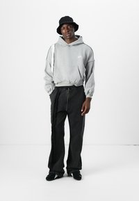 Grå oversized hoodie med en frontlomme, der har et slidt design. Matchet med sorte bredbenede bukser med en lynlåsdetalje. Sort bucket hat.