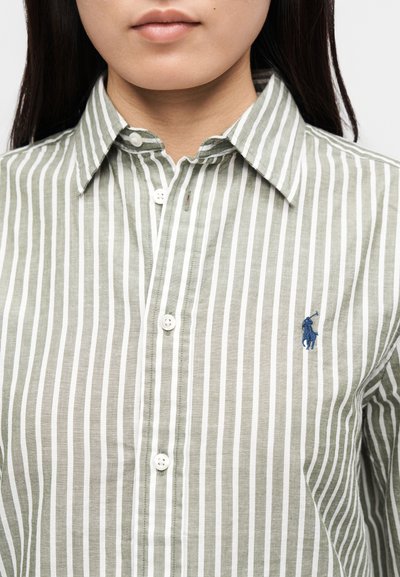 Zelená a biela pruhovaná košeľa na gombíky vyrobená z ľahkej tkaniny, s golierovým výstrihom a malým modrým logom na hrudi.
