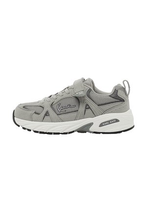 Chaussure de sport grise avec une tige en daim et en maille, dotée d'une sangle Velcro, d'accents texturés et d'une semelle intermédiaire blanche avec une semelle extérieure noire.