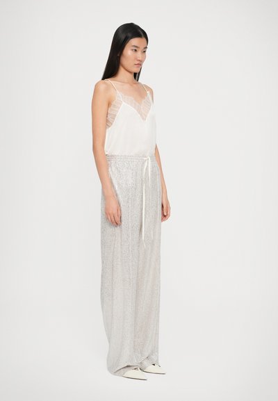 Top de satin alb cu panouri transparente cu volane; pantaloni largi argintii, strălucitori, cu talie ajustabilă; pantofi balerini ascuțiți.