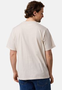 Krämfärgad bomull t-shirt med korta ärmar, avslappnad passform, synlig sömnad och subtil textur, visad från baksidan.