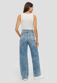 Jeans blu in denim a vita alta e gamba larga, con una consistenza morbida e un leggero motivo sbiadito, abbinati a un top bianco semplice senza maniche.