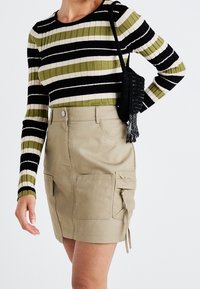 Pruhovaný žebrovaný top s dlouhým rukávem v černé, olivové a krémové barvě; doplněný béžovou sukní s kapsami na bocích a nastavitelnými šňůrkami.