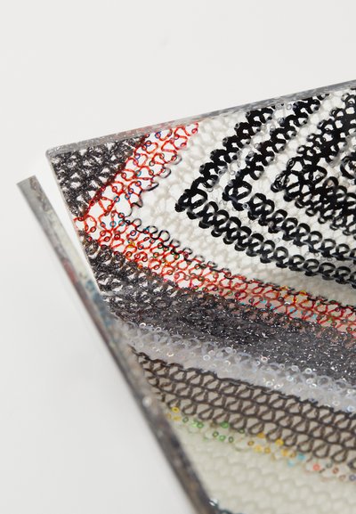 Pochette textile multicolore présentant des motifs complexes en fils noirs, rouges et blancs sur un fond transparent ; texture douce.