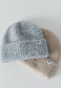 Two textured knit beanies, one light gray and one beige, each with a small white tag featuring a black logo.