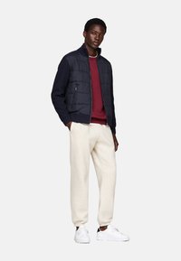 Chaqueta puffer navy con cremallera, sudadera burdeos debajo, pantalones de chándal crema y zapatillas blancas. Diseño simple y moderno con texturas superpuestas.