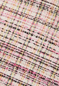 Gros plan d'un tissu tissé avec un motif à carreaux multicolores en fils roses, noirs, blancs, dorés et bleus.