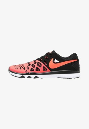 Zapatilla deportiva con parte superior de malla coral, superposiciones negras, swoosh de Nike coral, entresuela blanca y suela de goma negra, vista lateral.