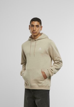 Beige hette med snøring, frontlomme og brodert logo. Har en avslappet passform og myk tekstur, kombinert med mørke jeans.
