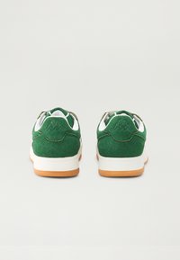 Tenis de camurça verde com detalhes brancos e sola de borracha natural, apresentando um patch de logo no calcanhar e um colarinho acolchoado para maior conforto.