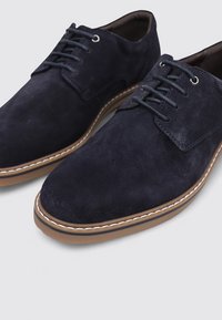 Zapatos de ante azul marino con punta redondeada, costuras detalladas y suela de goma marrón clara. Presentan un cierre tradicional con cordones.