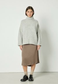 Pull grigio chiaro, lavorato a maglia spessa, con collo alto e orlo a coste; abbinato a una gonna marrone di lunghezza media e scarpe stringate nere.