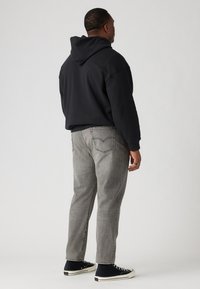Sudadera con capucha negra, jeans grises y zapatillas altas negras. Los jeans tienen un corte clásico con un acabado deslavado y detalles en el bolsillo trasero.