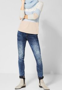 Ljusblå, creamfärgad och beige randig tröja; mörkblå denimjeans med ett blekt tvätt; beige ankelstövlar med svarta accenter.