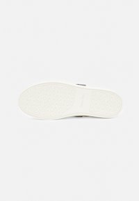 Schuhsohle aus weißem Gummi mit texturiertem Muster, das kreisförmige Motive und "Calvin Klein"-Markenlogo zeigt. Glatte Oberfläche, flexibles Design.