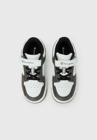 Λευκά και γκρι παιδικά αθλητικά παπούτσια με μαύρα κορδόνια, λουράκια βέλκρο με την ετικέτα "Champion" και οπές στην περιοχή των δακτύλων, με θέα από πάνω.