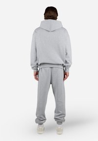 Light gray cotton sweatshirt with hood, oversized fit, and ribbed cuffs. Paired with matching sweatpants featuring elastic ankle cuffs.