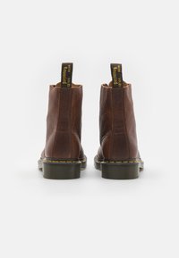 Bottines en cuir brun avec une finition texturée, des coutures jaunes et des languettes de tirage. Dotées d'une épaisse semelle en caoutchouc nervurée.