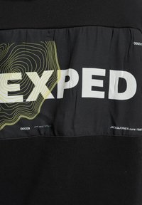 Svart hettegenser med trykt hvit tekst "EXPED" og gule topografiske linjer. Glatt stoff med design for å ta på seg over hodet og kontrasterende nederste del.
