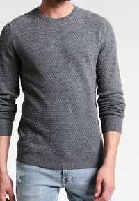 Pull en maille gris avec un motif losange texturé, col rond, poignets et ourlet côtelés, associé à un jean bleu clair déchiré.
