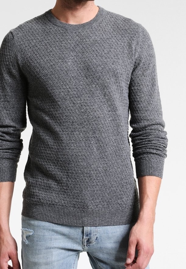 Pull en maille gris avec un motif losange texturé, col rond, poignets et ourlet côtelés, associé à un jean bleu clair déchiré.