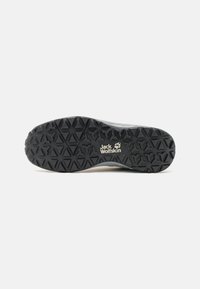 Semelle de chaussure noire avec motif de bande de roulement triangulaire texturé et logo "Jack Wolfskin" avec empreinte de patte au centre, sur fond blanc.