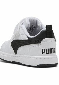 Baskets blanches synthétiques avec un accent en cuir noir et une sangle velcro. Comprend un col rembourré et un logo "PUMA" bien visible à l'arrière.