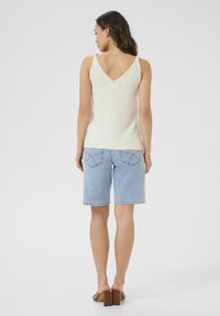 Light beige sleeveless top with a V-neck and soft texture, paired with light blue denim shorts featuring back pockets and stitched accents.