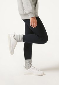 Marinefarbene Leggings, kombiniert mit hellgrauen Socken und weißen Sneakers mit drei Klettverschlussriemen. Weiches, dehnbares Material mit glatter Textur.
